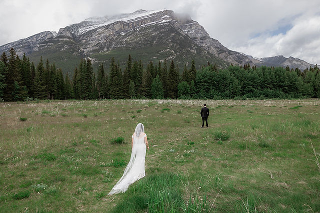 Bride walking toward groom for first look in a grassy area with Rocky Mountains in the scene 