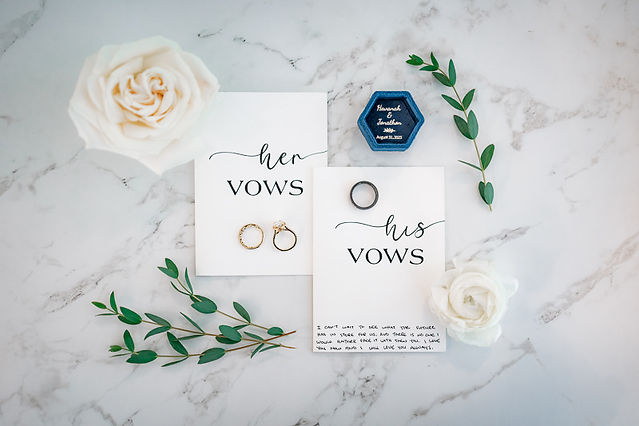 Flat lay of his and her vows, white roses, eucalyptus, royal blue ring box