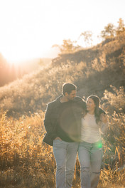 Couple walking together through tall grass at golden hour during a Calgary engagement photographer session.