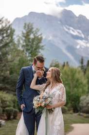 Bride and groom sharing a playful, romantic moment during their Canmore Nordic Centre wedding, with the bride holding her bouquet beneath the dramatic Rocky Mountain peaks.