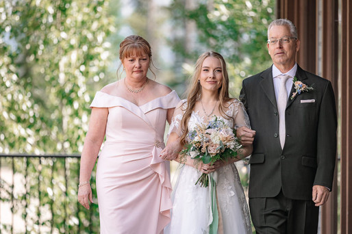 Bride walking down the aisle with her parents during an outdoor ceremony at one of the beautiful Canmore wedding venues, holding her bouquet as guests await beneath the Rocky Mountains.