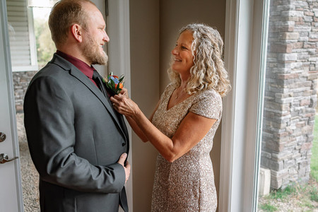 Mother helping the groom with his boutonniere during an emotional getting ready moment before a romantic farm wedding.