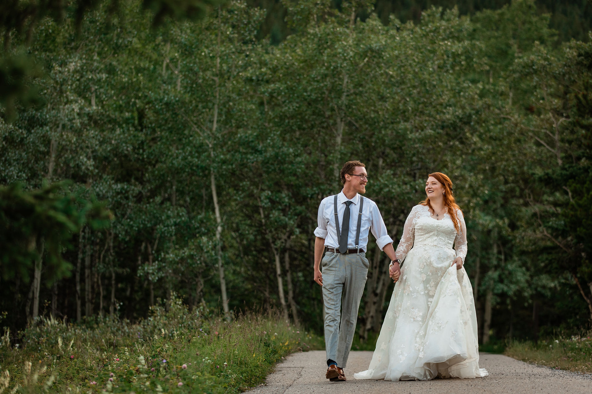 Bride and groom walking hand in hand on a tree lined pathway.