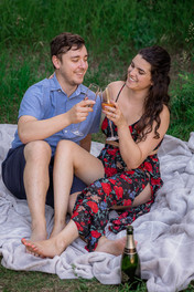 Couple sitting on a picnic blanket outside while toasting their engagement
