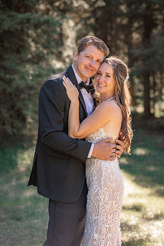 Bride and groom holding each other and smiling during their wedding portraits in a forest setting at one of the beautiful Cochrane wedding venues.