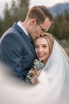A Canmore wedding photographer captures the groom kissing the bride's forehead as she smiles toward the camera.