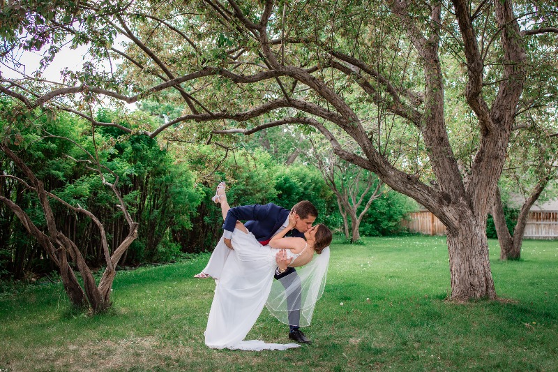 bride and groom dip kiss in the yard under the trees