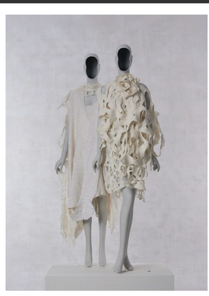 This look is a multi layered ensemble of a draped asymmetrical dress, a hand felted cashmere scarf that transports us to the natural world and sea life as well as a sculptural elliptical asymmetric  scarf around one shoulder for a dramatic effect. The base material of the dress is silk charmeuse which is lined and hand felted with ultrafine merino wool fibers. The white hand felted fiber panels are draped diagonally to form an asymmetrical dress which is luxuriously soft and lustrous. The Cashmere web scarf transports us to sea and oceanic creatures forming organic shapes in net like formation and undulating waves floating over the neck and falling to the back of the dress. On the other shoulder is a silk merino loop scarf with organic forms giving it a fluid and sculptural form. For this look I was inspired by the asymmetric forms in nature that are prevalent and celebrated as a form of beauty in art but feared and excluded in society and culture. By using my strengths to fashion the body as a visually impaired person, I invite audiences to celebrate the unique life experiences that disability brings to our society. Embodying asymmetry and organic forms through dress is my way of challenging what we conventionally understand as beauty in human form and existence. 
This look consists of four layers of hand felted ultrafine merino wool(14.5 micron) and mulberry silk fibers in tactile-visual gradations of the holes built into each layer. Each layer is hand crafted using a hand felting method and does not have any seams. They can be layered in multiple ways to create multiple iterations in shape and form. The juxtaposition of the patterns that the holes make as well as the layering of the hand felted merino textiles that shape the body create layers of floating holes that add drama and tactile variation. The gradation is a visual phenomenon but this piece challenges this sight oriented understanding of undulation of color and texture to be understood via tactile interpretation of the material that is luxurious, light and soft to touch. On top of the four layers lies a flower shaped neck accessory also made with ultrafine merino wool and mulberry silk fiber with a hand felted cord as a choker for the neck and base for the flower. This look invites the viewer to reflect on the embodied experiences of people who are blind and have low vision as contributors and innovators in an ocular centric world. The natural cream tones of the fibers reflect the artist’s experience as a person with Albinism.

