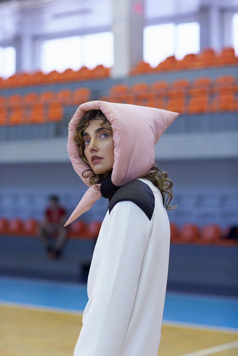 Beautiful white fashion model wearing a pink hat with a white top stands in a basketball court.