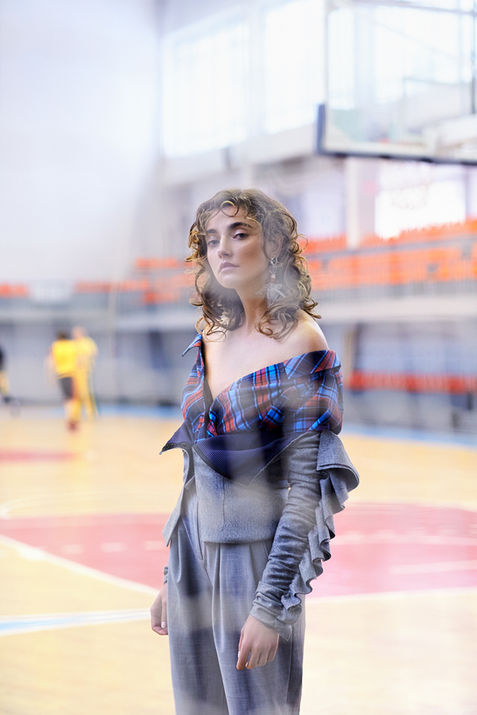Beautiful white fashion model wearing a top with tartan detail stands in a basketball court.