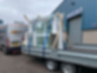 A delivery van and trailer carry large glass panels secured with straps