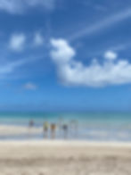 Praia de Antunes (Antunes Beach). A white sand beach in the foreground, with hammocks in the middle, and bright blue water behind. There are clouds in the sky, but the weather looks warm and inviting.