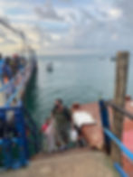 The image is of a water taxi which has docked in Morro de Sao Paulo. In the picture, you can see the narrow, rusty stairs which allow passengers to disembark from the water taxi onto the dock.