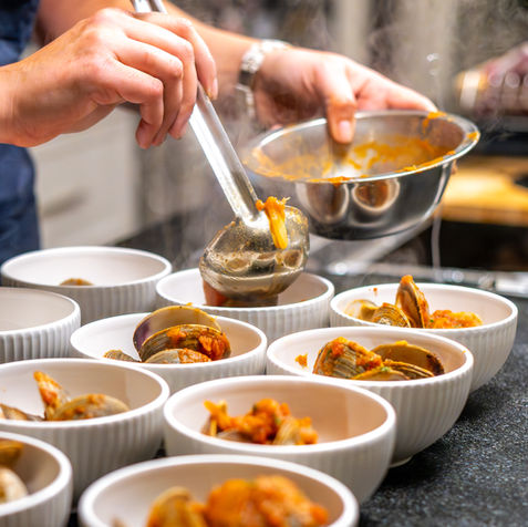 Hands plating seafood into bowls in warm kitchen light, behind the scenes food photography