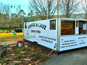 Coffee N Cruz drive-thru kiosk in a park, with COFFEE sign, cashless cards-only notice, and mushroom decor.