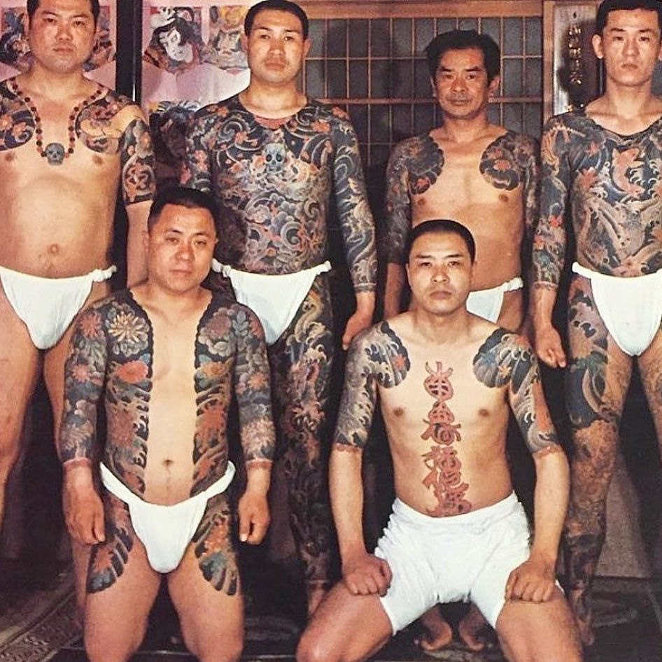 Groupe d’hommes japonais arborant des tatouages traditionnels irezumi couvrant le torse, le dos et les bras, réalisés avec des motifs complexes et colorés.