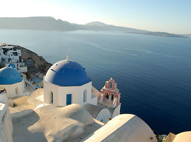 Classic blue-domed churches of Oia, Santorini, set against the backdrop of the Aegean Sea at sunset.