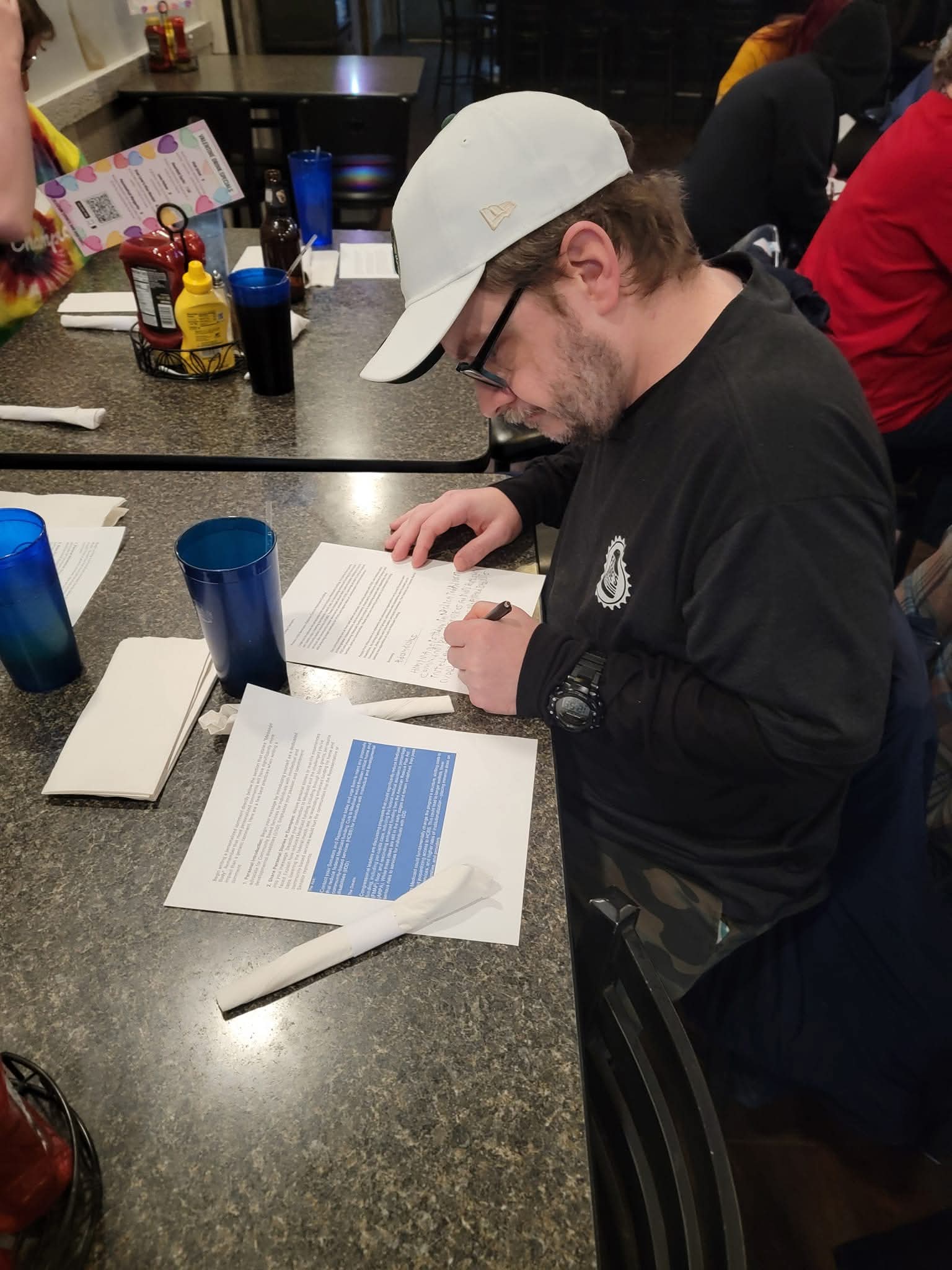 A man wearing a hat and glasses is looking at materials to write a letter to legislators.
