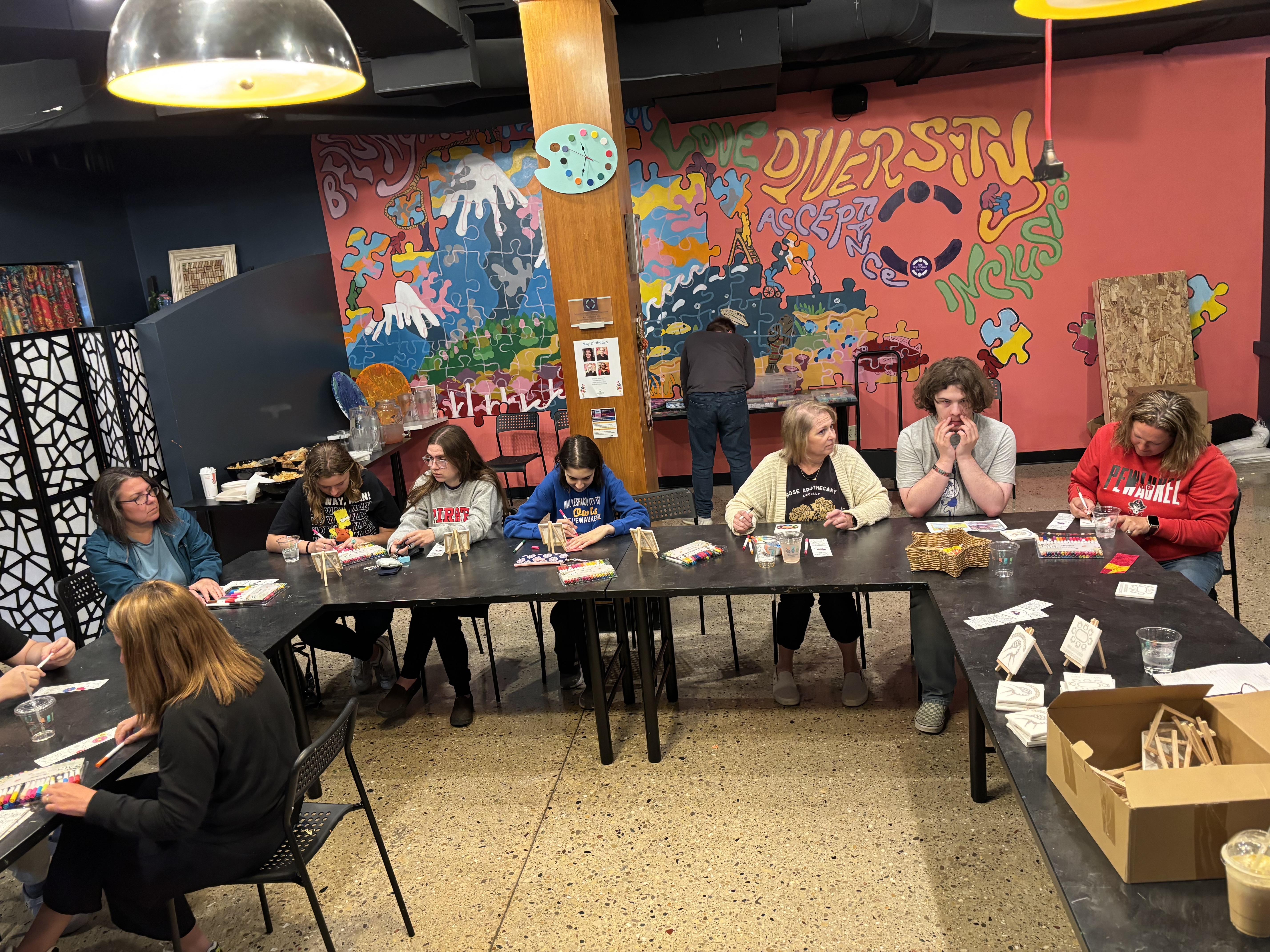 Young people seated at a U shaped table in front of a colorful mural.