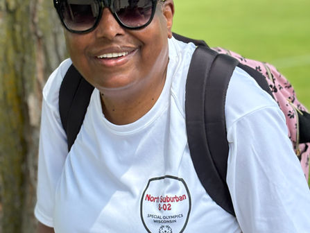 A smiling African American woman in a cap stands outside. She is wearing a Special Olympics shirt.