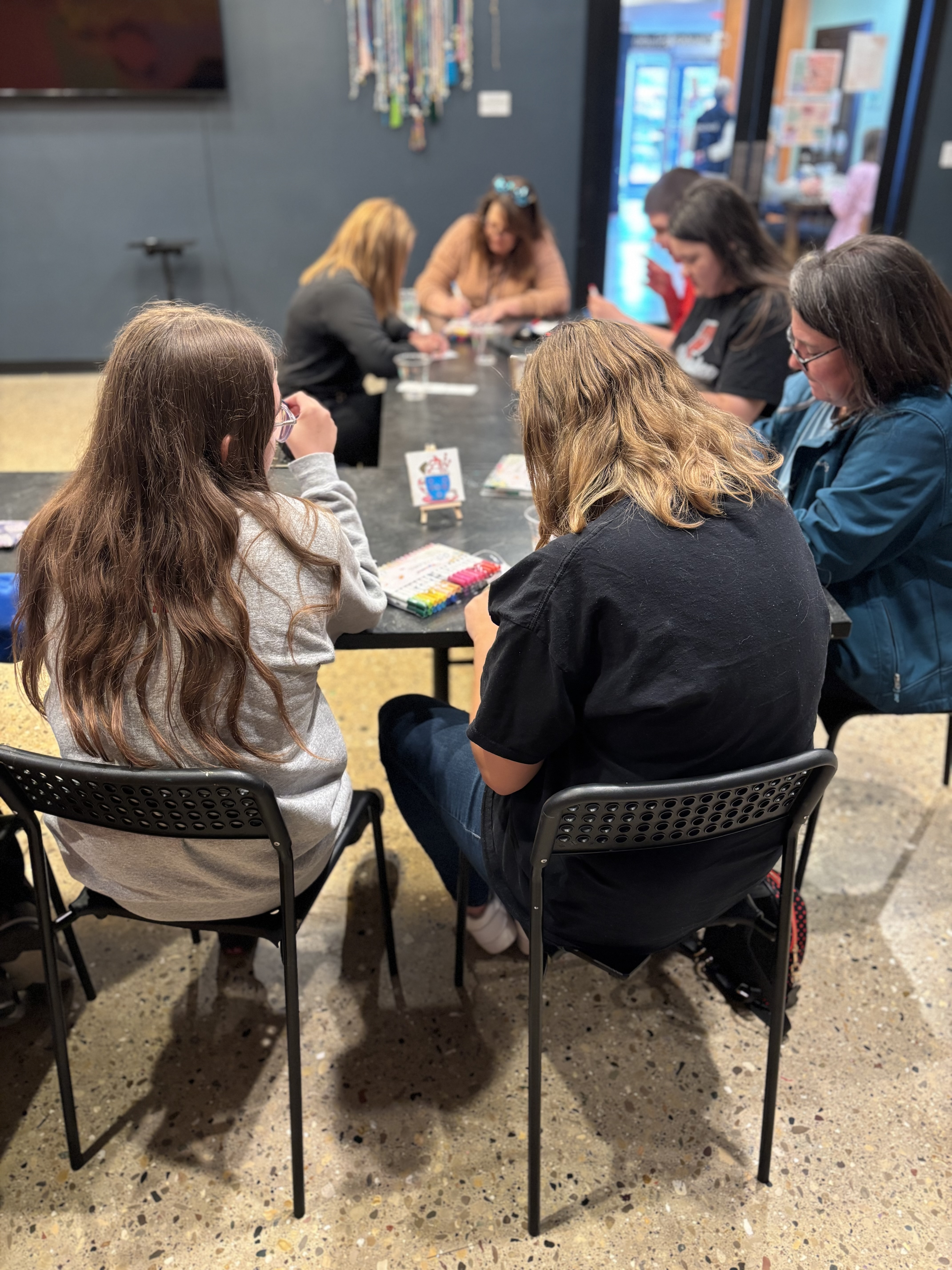 Young people  seated at a table looking down as they make friendship bracelets.