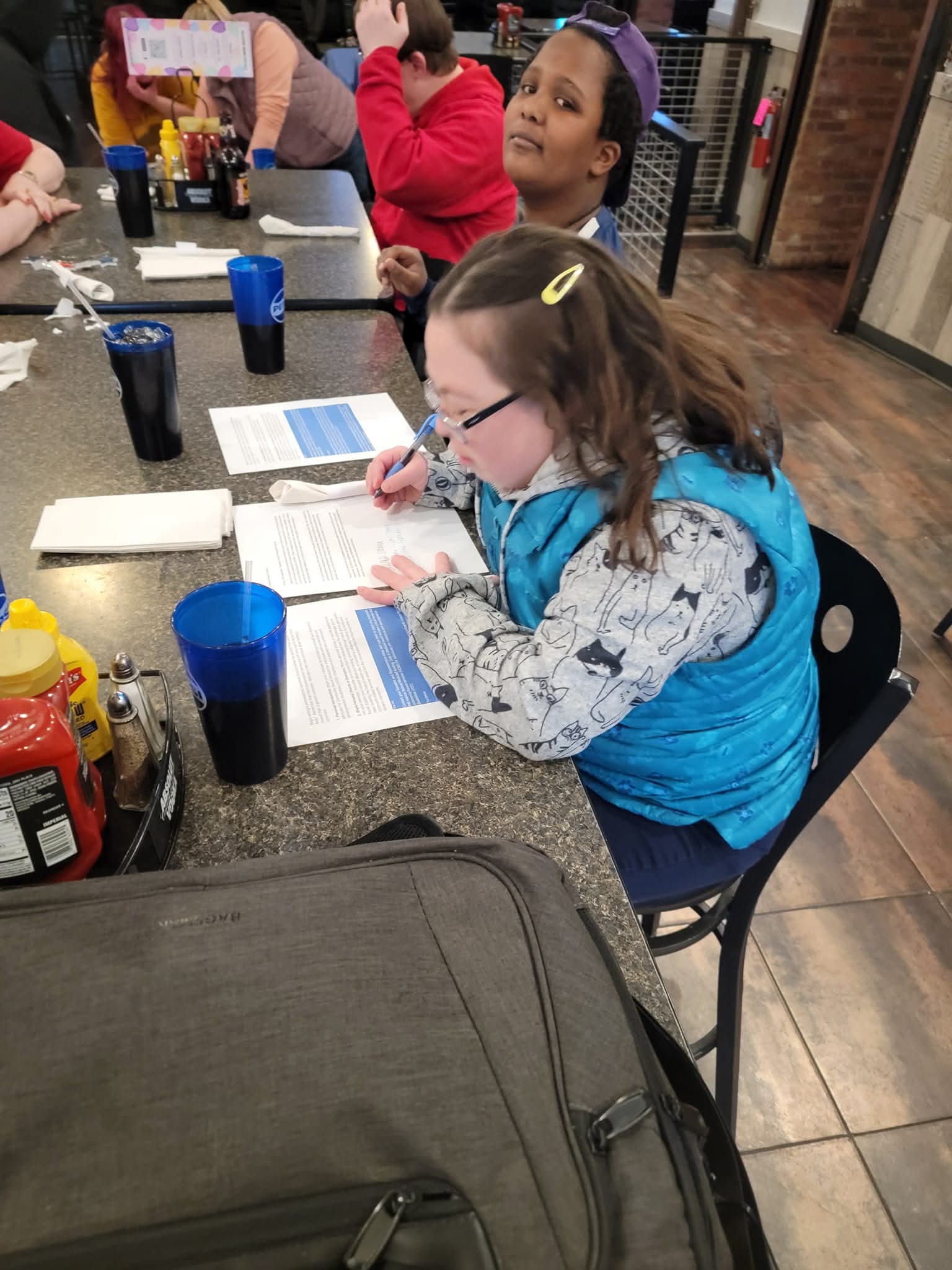 A young woman is seated at a table looking down and writing.