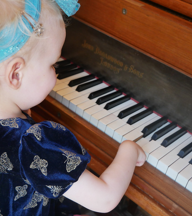 Young child sitting at a grand piano with one hand on the keys.