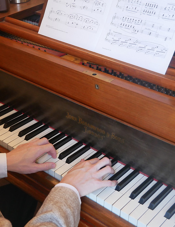 Hands playing a grand piano beneath open sheet music.