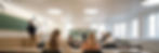 Children sit at desks in a bright classroom with large windows and Full Spectrum LED lights. A teacher writes on the blackboard. The mood is focused and studious.