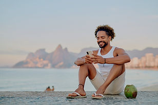 Homme souriant avec téléphone, bord de mer et montagnes