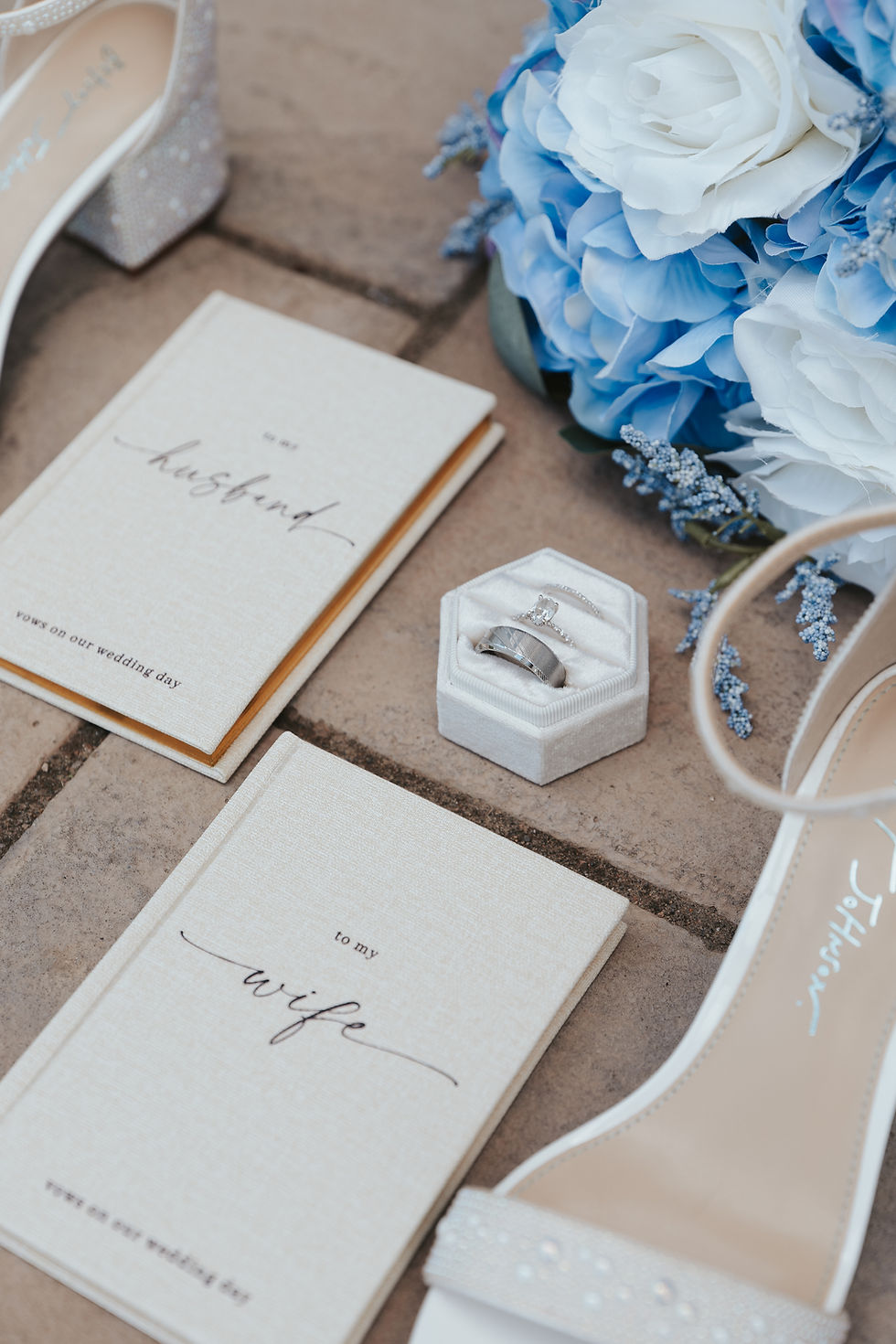 Wedding details on stone at luxurious West Virginia wedding venue: vow books "to my husband/wife," rings in box, blue and white bouquet, white shoes. Elegant and romantic.