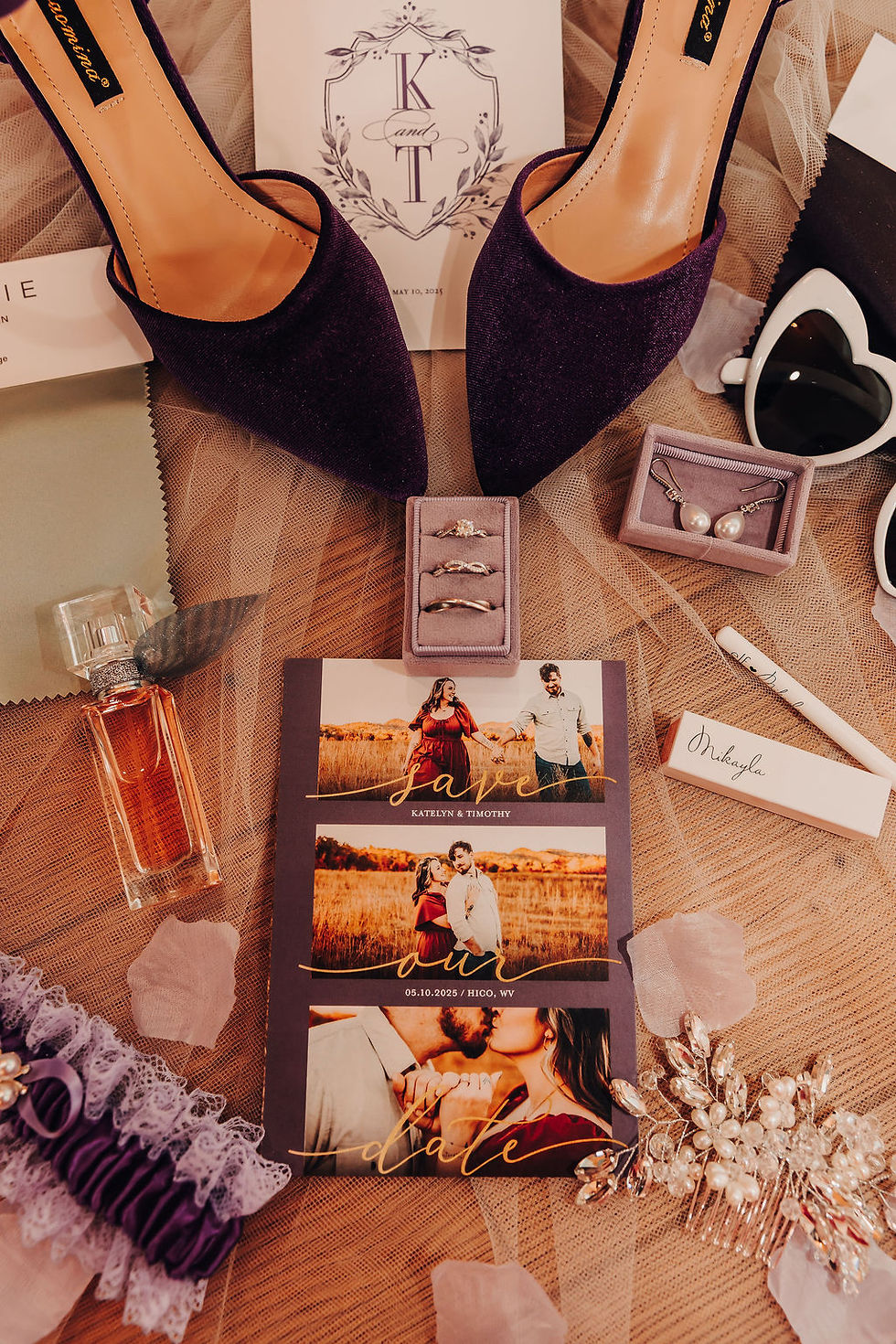 Wedding items laid out: purple shoes, invitation with "K & T," rings, necklace, photos, perfume, sunglasses, and wedding date card at luxurious West Virginia wedding venue.