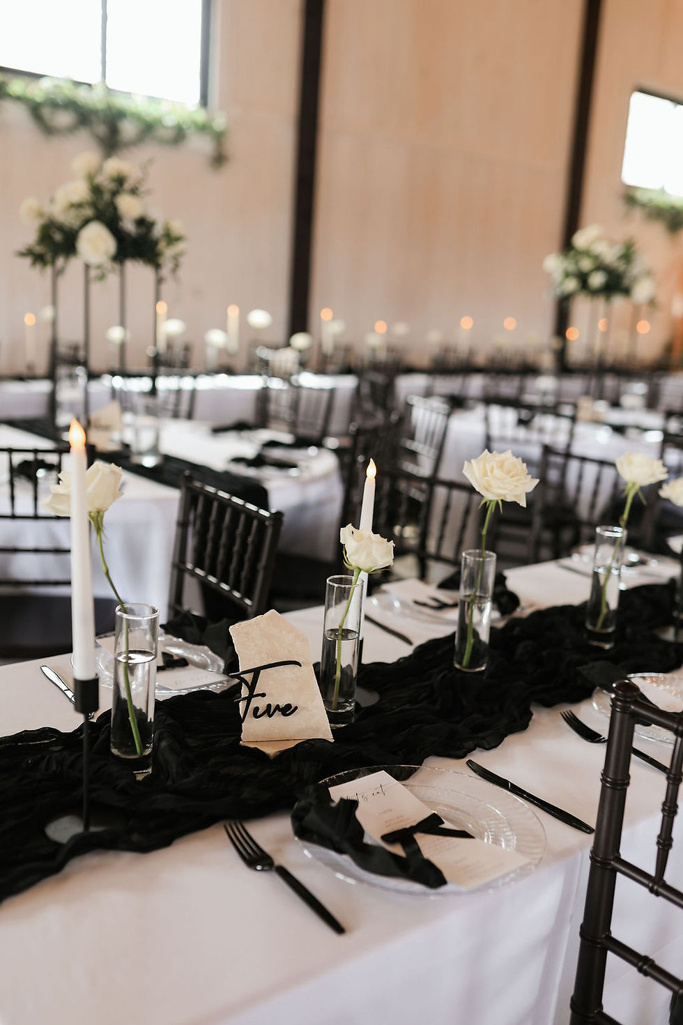 Elegant dining table set for an wedding with white roses, black accents, candles, and a "Five" table number at stunning Charleston, WV wedding venue. Soft, warm lighting and refined mood.