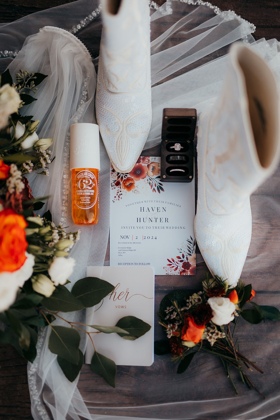 Wedding detail flat lay with white boots, floral bouquet, vows booklet, orange bottle, rings, and an invite reading "Haven Hunter, Nov 2, 2024" at luxurious West Virginia wedding venue