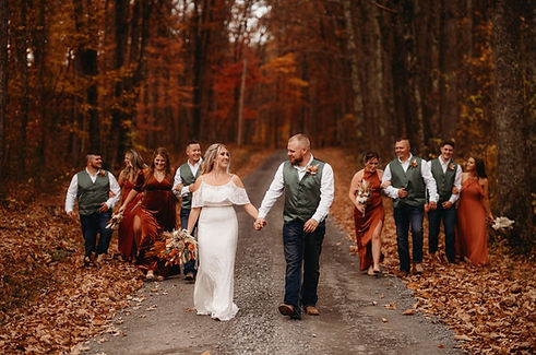 bride and groom walk down gravel road while holding hands during beautiful fall wedding with wedding party surrounding them at wedding reception venue in West Virginia