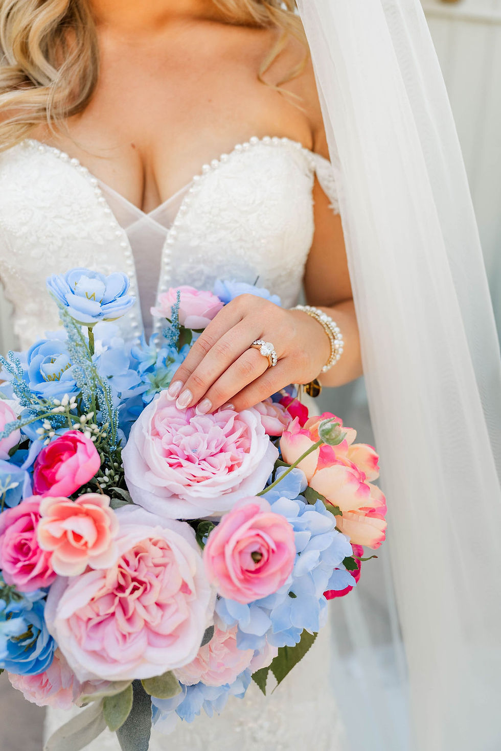 Bride in a white beaded wedding dress and veil holds a pastel pink, blue, and peach bouquet, showing her engagement ring and nails at a wedding venue in Charleston, WV.