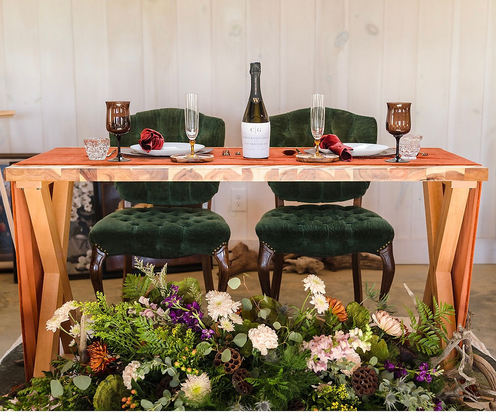 Elegant sweetheart table setup at Charleston, WV wedding venue with green chairs, a wooden table, wine bottle, and glasses. Floral arrangement in front, warm and inviting ambiance.