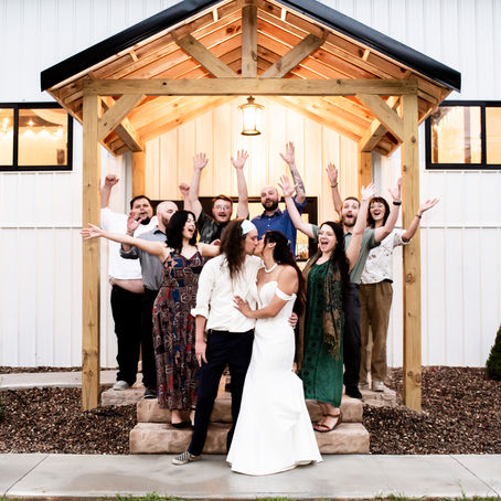 Bride and groom kiss under a wooden gazebo, surrounded by cheering friends. White wedding venue in Charleston, West Virginia in the background, joyful atmosphere.