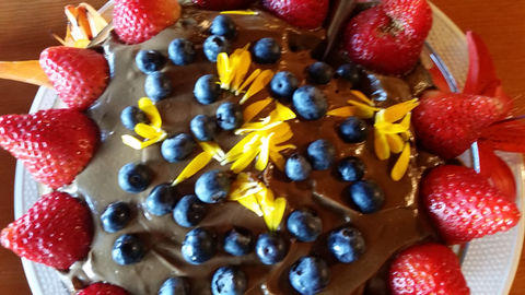 a chocolate cake with strawberries, blueberries and orange flower petals arranged on top as decoration
