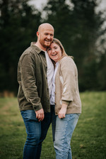 Parents hugging and smiling in the woodland light.