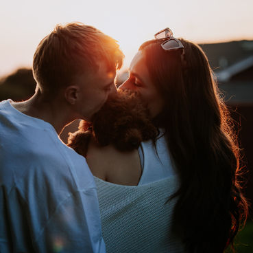 Portrait of a couple kissing a puppy at sunset