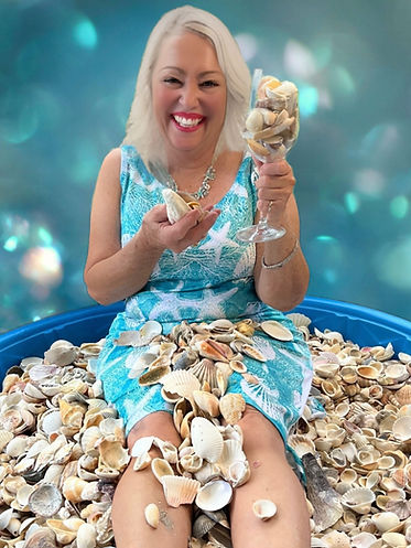 Beatriz Valiente, artist and designer at Caracola Creations, sitting in a kiddie pool filled with seashells.