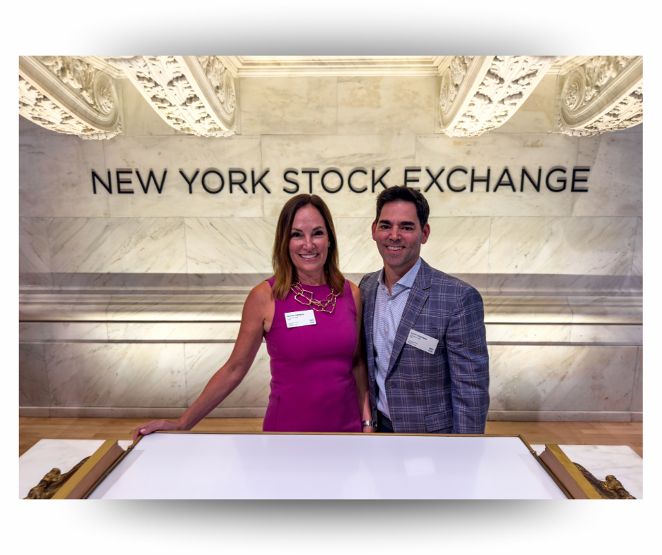 A woman in a pink dress and a man in a plaid jacket stand beneath the New York Stock Exchange sign.