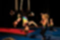 Two white aerial students, about age 6, high five each other. One is hanging upside down on a trapeze while the other stands on the ground, and both are smiling and laughing.