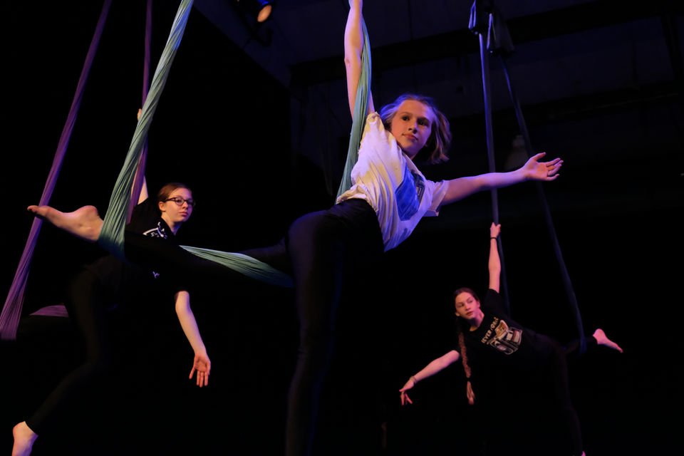 3 tween students pose while performing on aerial sling, one with blonde hair, one with glasses, and the third with a long brown braid.