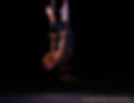 A white female bodied woman performs an arched bird's nest pose on a trapeze.