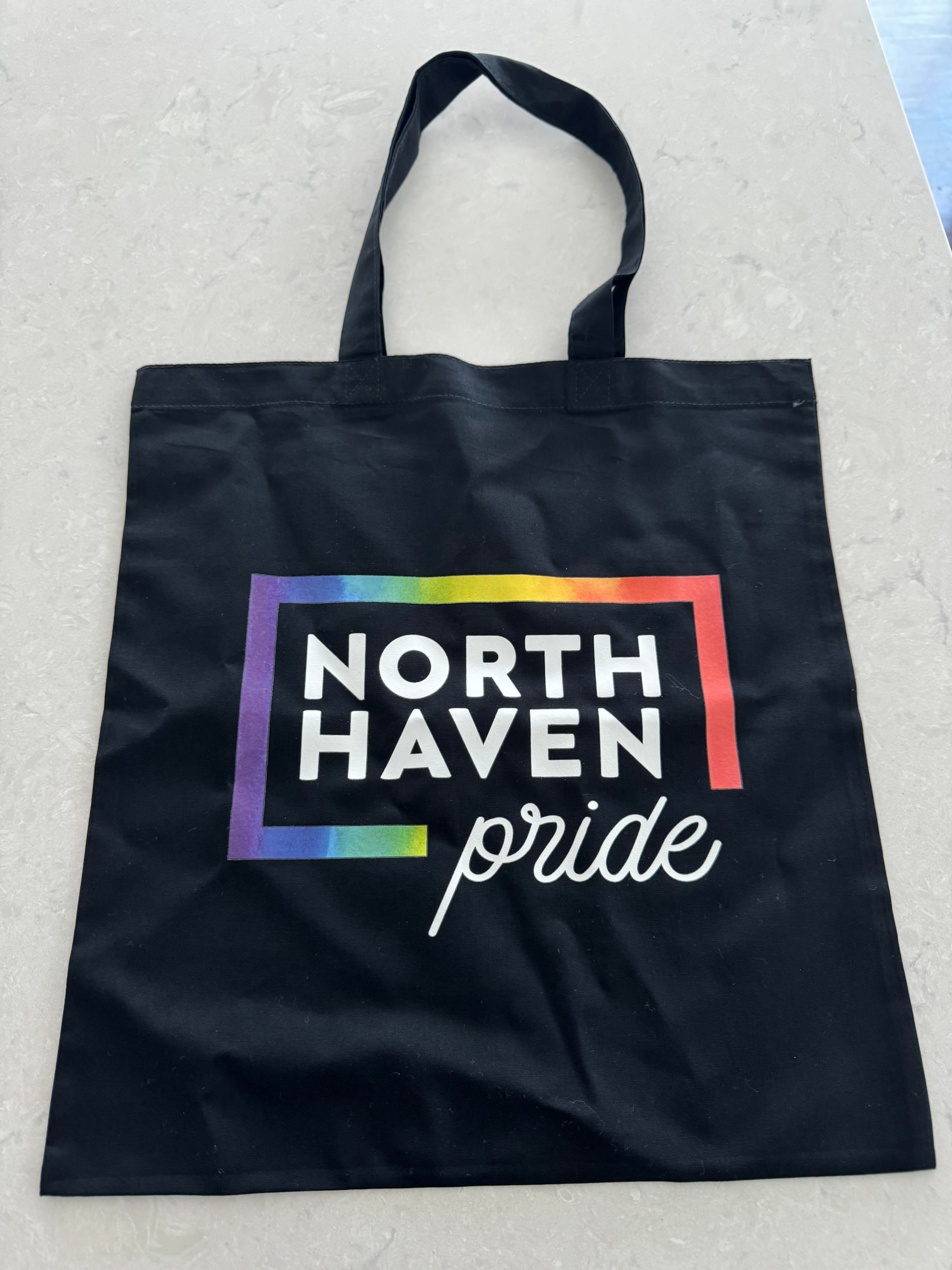 Black tote with North Haven Pride logo on it being held by a person