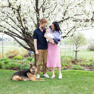 a couple holding a baby, with a dog lying the ground and white cherry blossom tree in the background