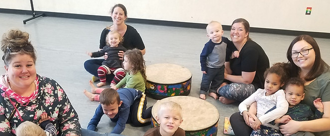 families with small children smiling in a group with gathering drums while seated on the floor