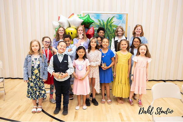 teenagers, children and a teacher posing in front of hawaiian themed decorations after a recital